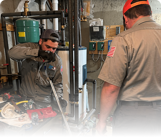 Two technicians in uniforms work on pipes and mechanical equipment in a utility room, surrounded by tools and machinery, ensuring reliable Denver heating solutions.