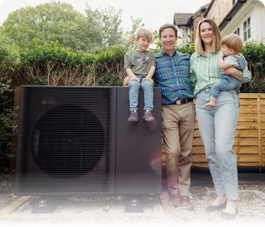 A family of four stands outside next to a large black heat pump unit; one child sits on the unit while the other is held by an adult, showcasing efficient Denver heating solutions for all seasons.