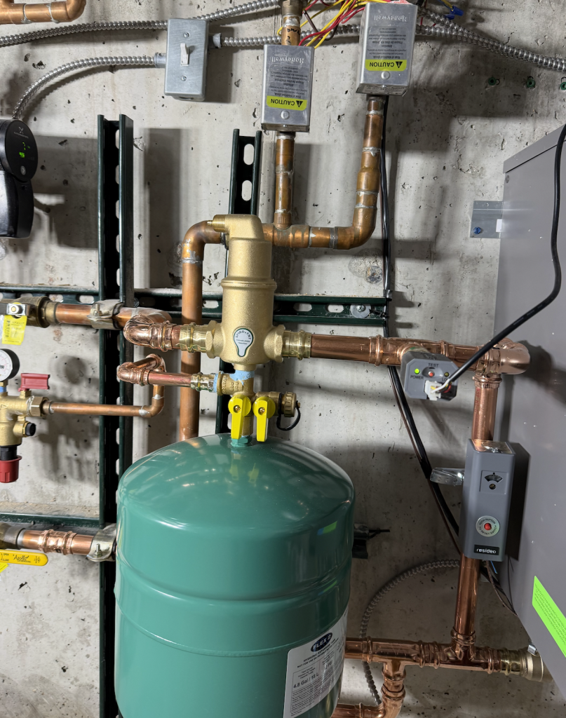 Lochinvar Noble 150 boiler Installed-1 Green expansion tank connected to copper plumbing pipes with shut off valves and control units mounted on a concrete basement wall.