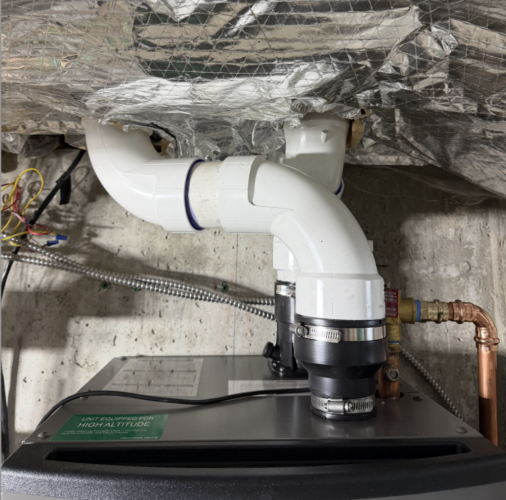 Lochinvar Noble 150 boiler Installed-1 A close up view of white PVC pipes connected to a HVAC unit, with insulation above and copper tubing visible to the right.